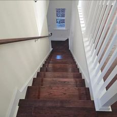 Dark wood staircase with white railing and wall, leading downwards.