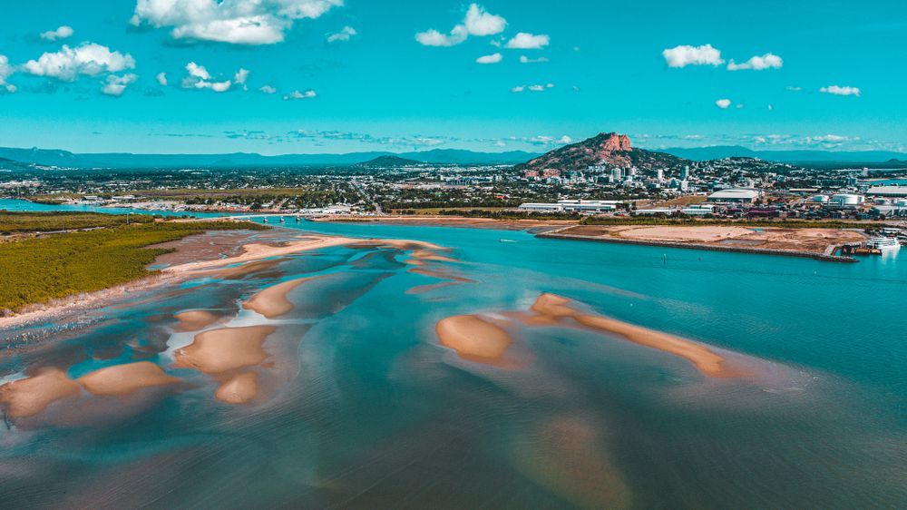 A Man Is Spraying a Field with A Hose Next to A River — Wades Distributors In Townsville, QLD