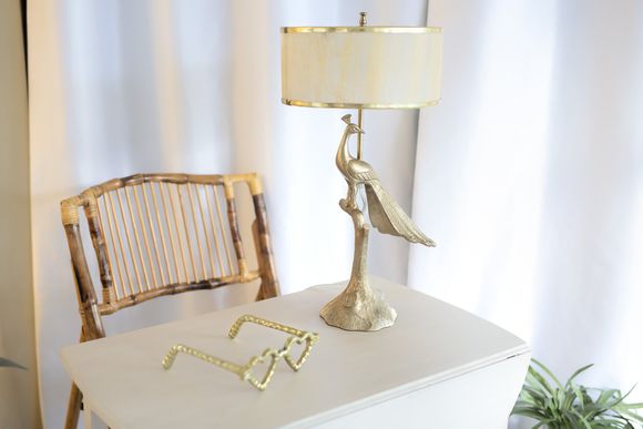 White table with gold lamp and bamboo chair against white curtains