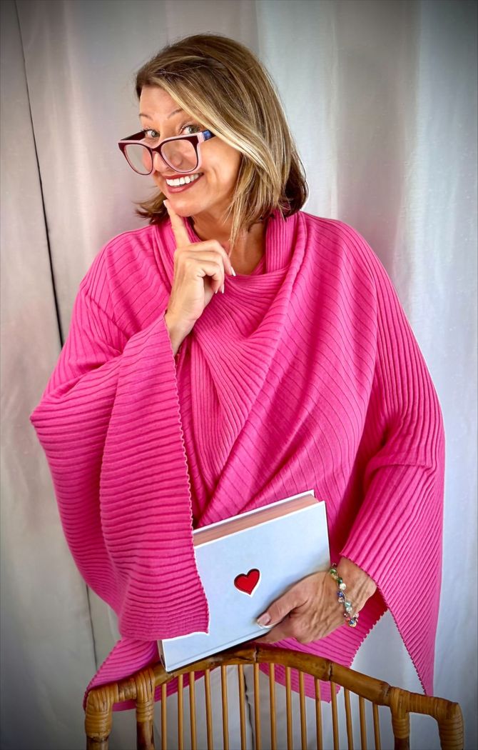 Woman in a bright pink sweater holding a notebook with a heart, smiling indoors
