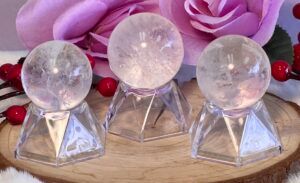 Three clear crystal balls on clear pyramid stands, with a pink rose and berries in the background.
