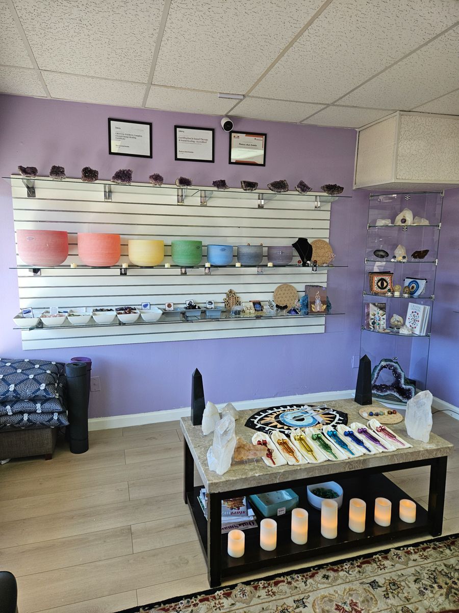 A crystal shop interior with shelves, display table, various colored crystals, and singing bowls.