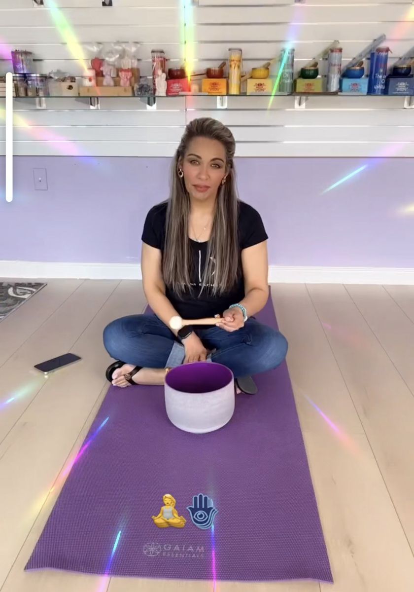 Woman seated on a yoga mat, holding a mallet near a singing bowl.