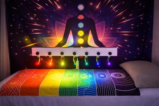 A therapy bed with rainbow-colored lights, chakra symbols, and a backdrop of a meditating figure with glowing chakra points.