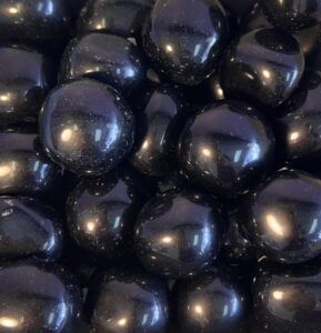 Pile of glossy, black, round candies, possibly jelly beans.