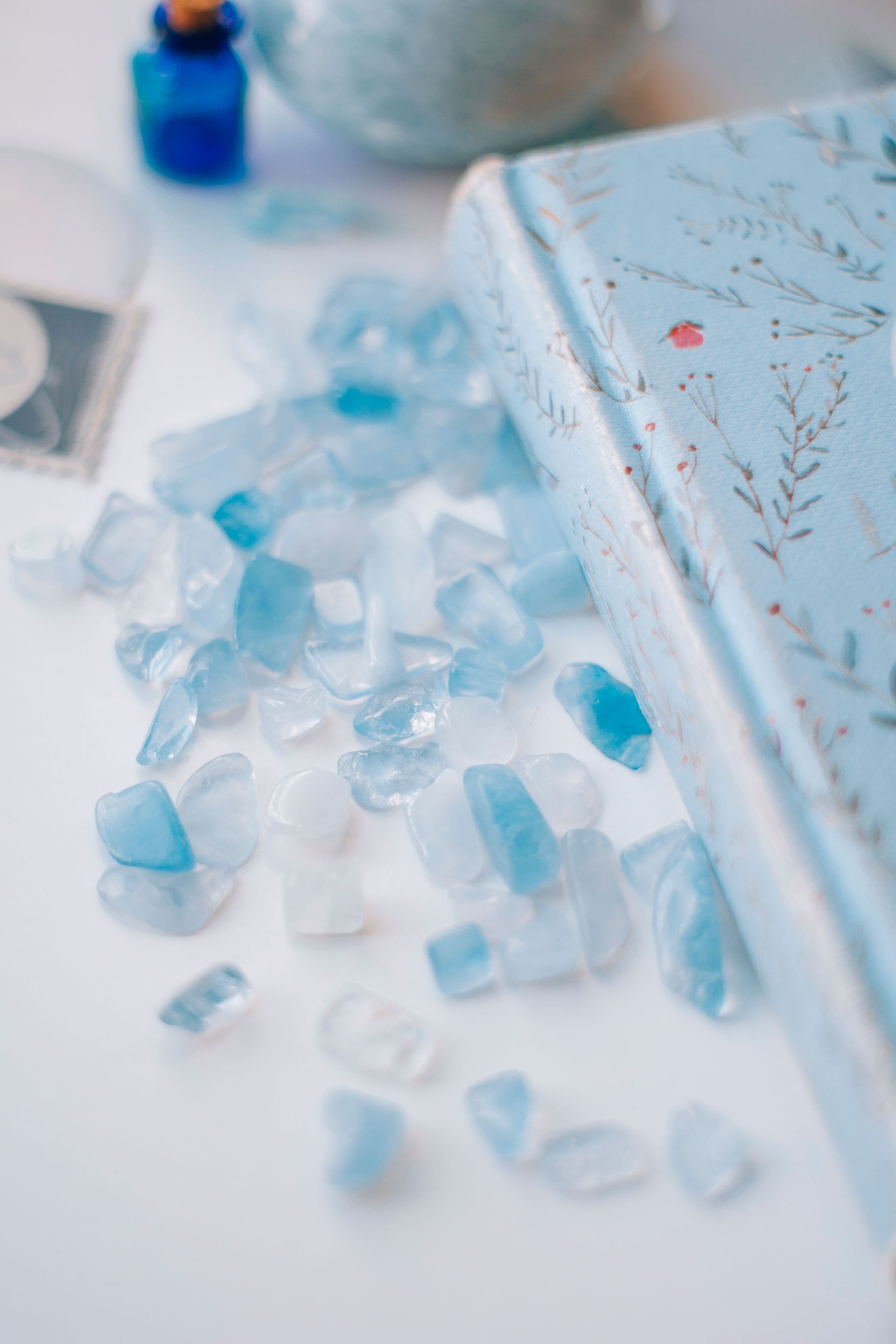 Blue glass crystals scattered beside a white tray with a soft blue bottle in the background