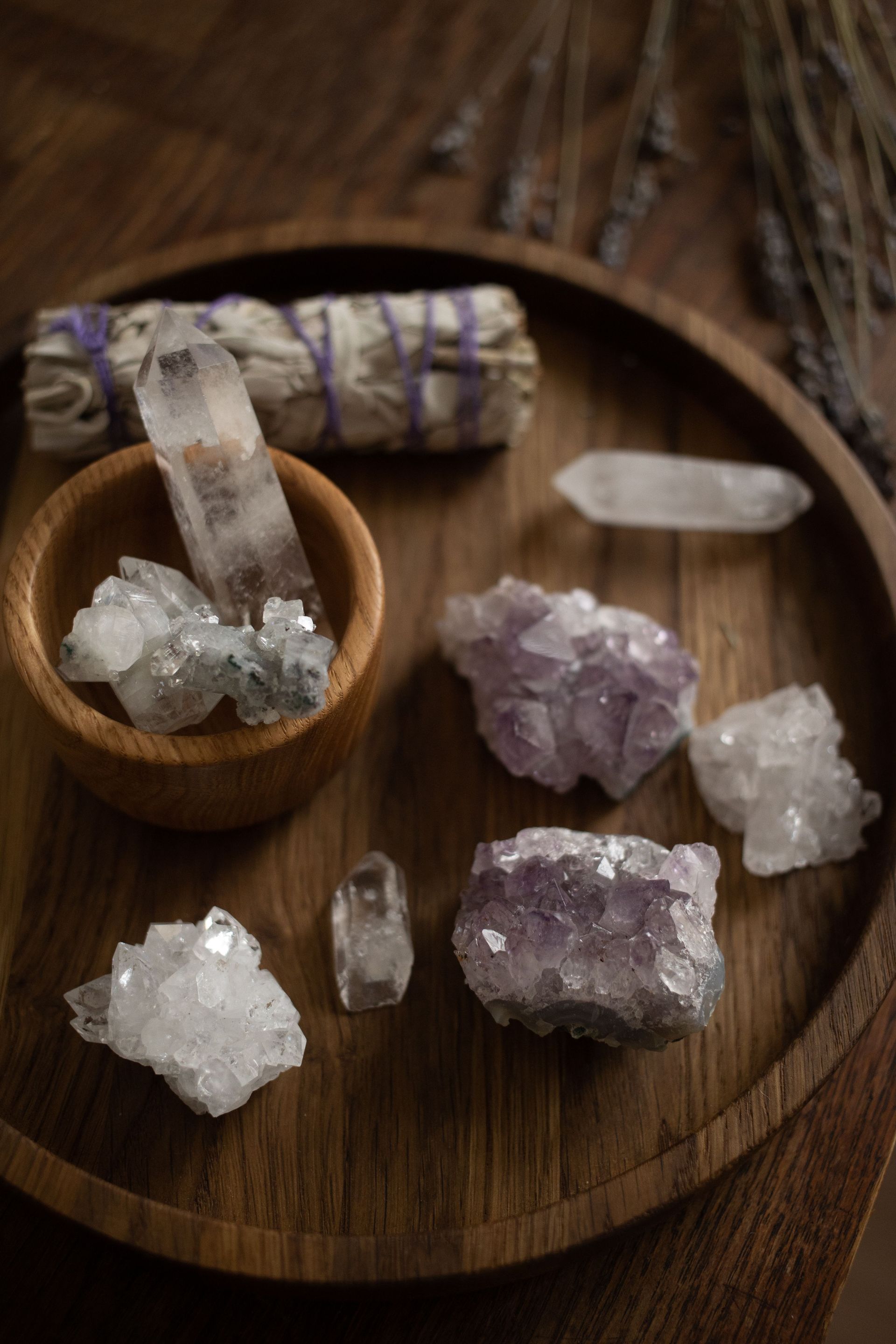 Clear and purple crystals arranged on a round wooden tray with a small bowl and rolled sage bundle