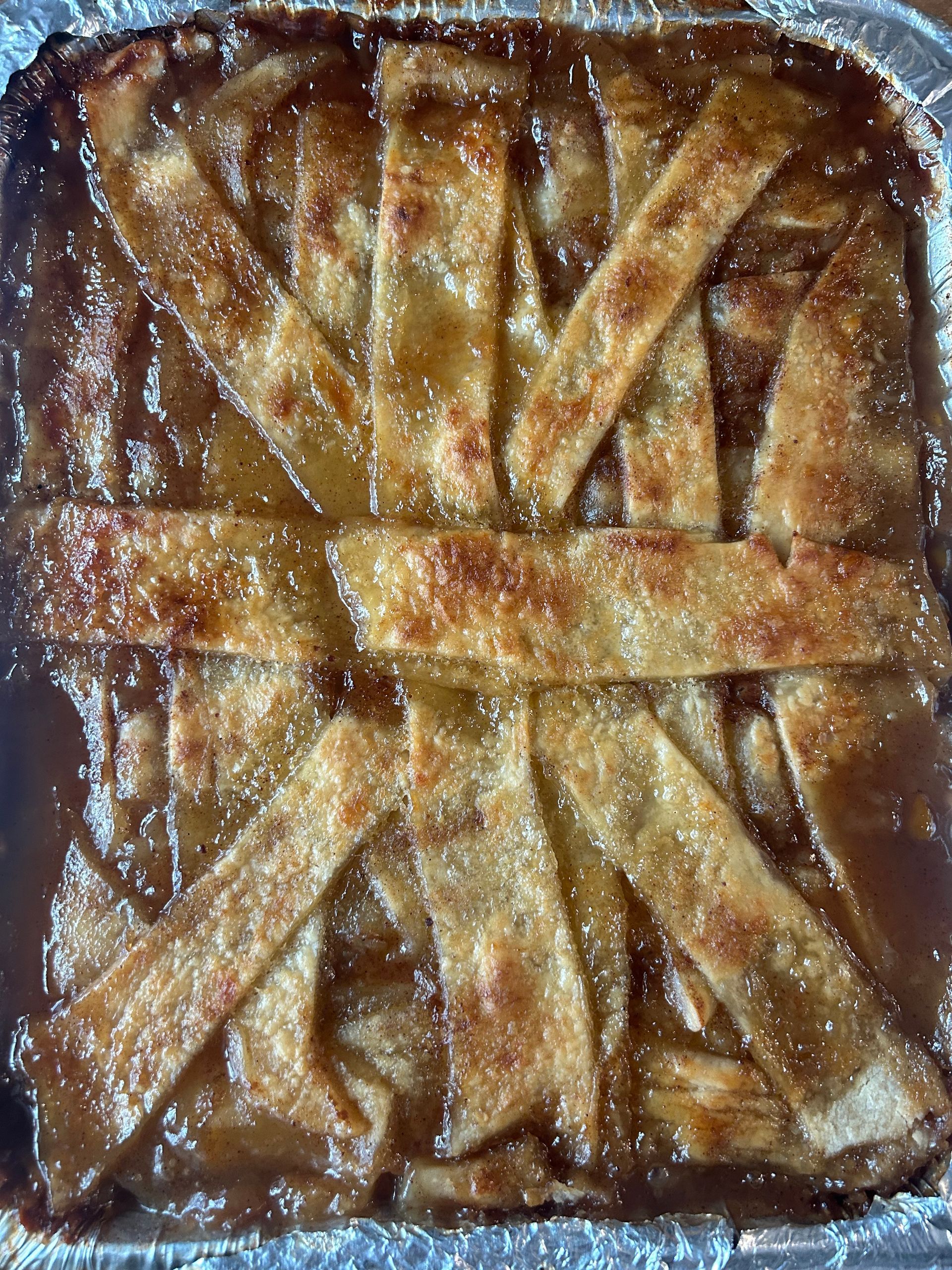 Apple pie in foil pan with a lattice crust, golden-brown.