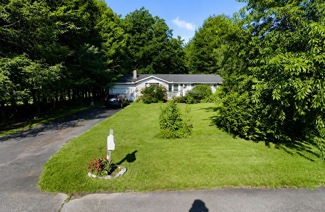 Single-story house with a large green lawn and trees on a sunny day.