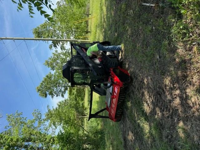 A red-and-black utility vehicle on a dirt path beside trees and power lines.