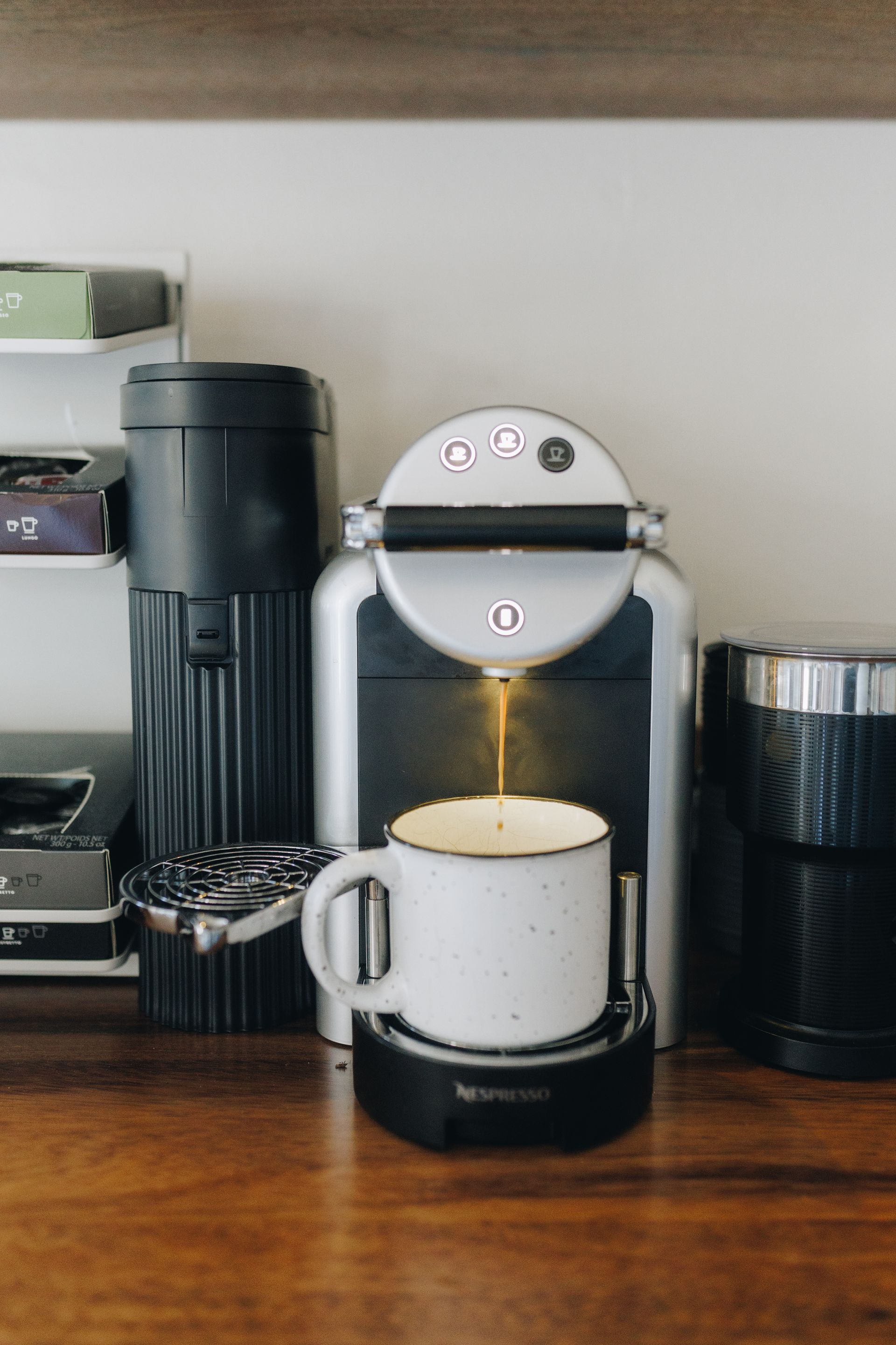 Countertop coffee maker brewing into a white mug on a wooden kitchen counter.