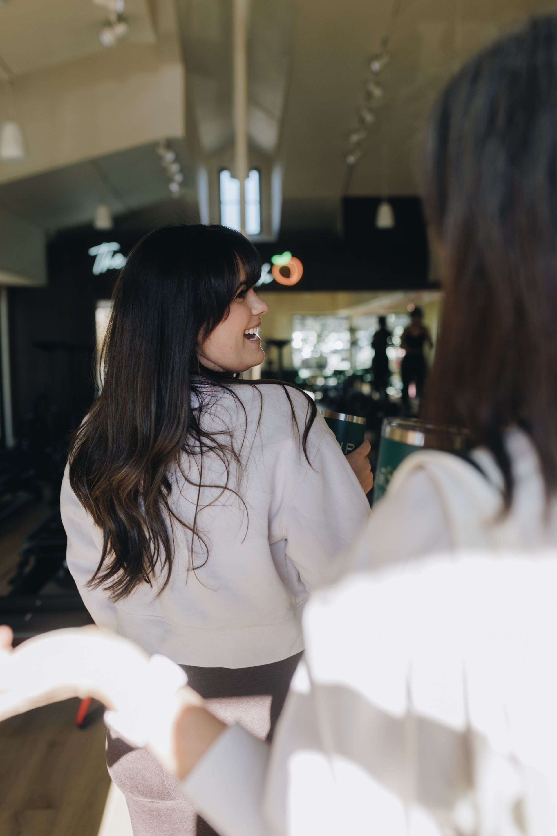 Two women sitting in a café, one turning back and smiling over her shoulder