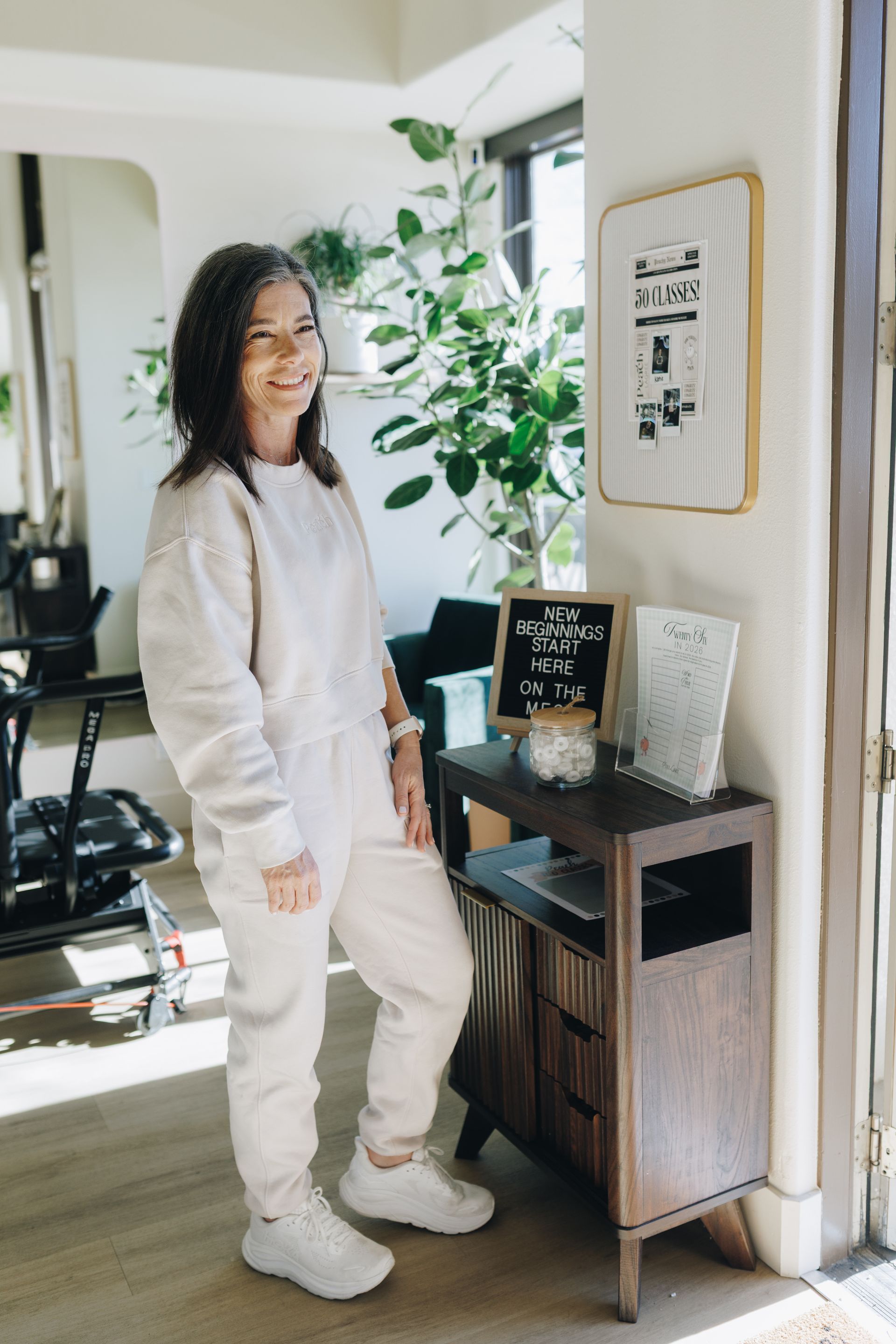 Woman standing beside a small console table in a bright entryway, with framed art and a potted plant nearby.