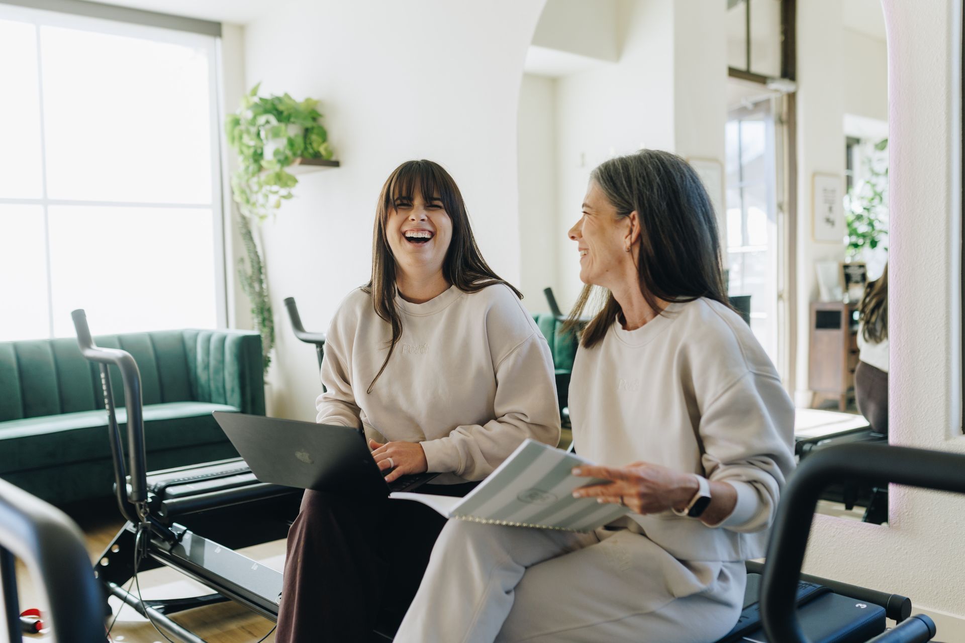 Two people chatting on a couch in a bright office, holding papers and smiling