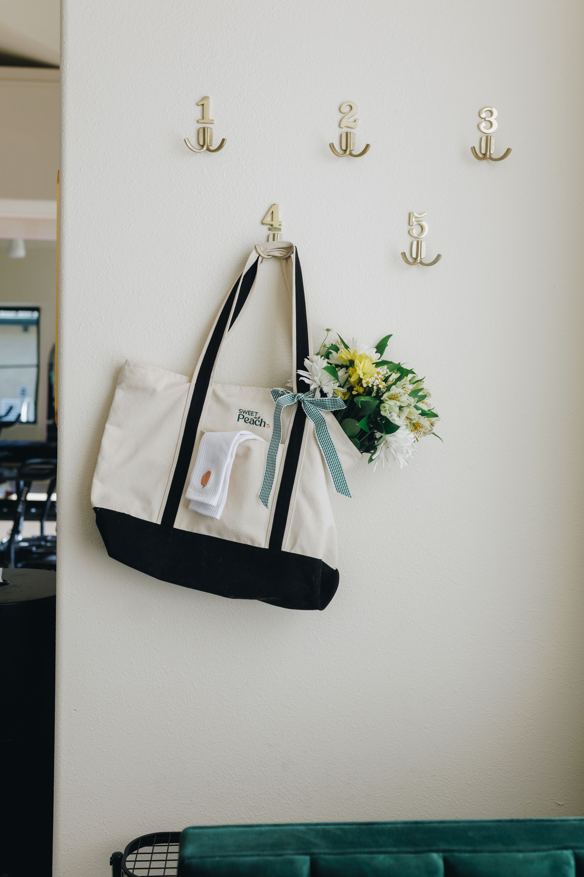 Wall hooks on a white wall holding a black tote bag and a bouquet of flowers.