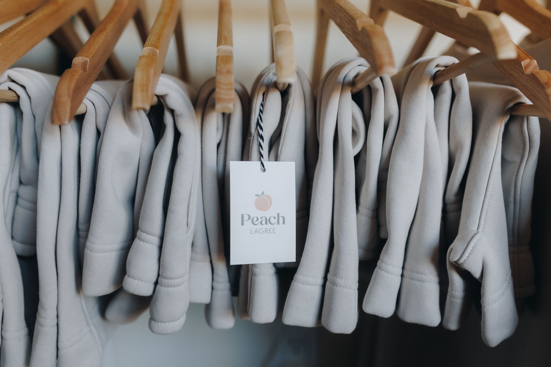 Row of light gray sweaters on wooden hangers with a white brand tag in the center