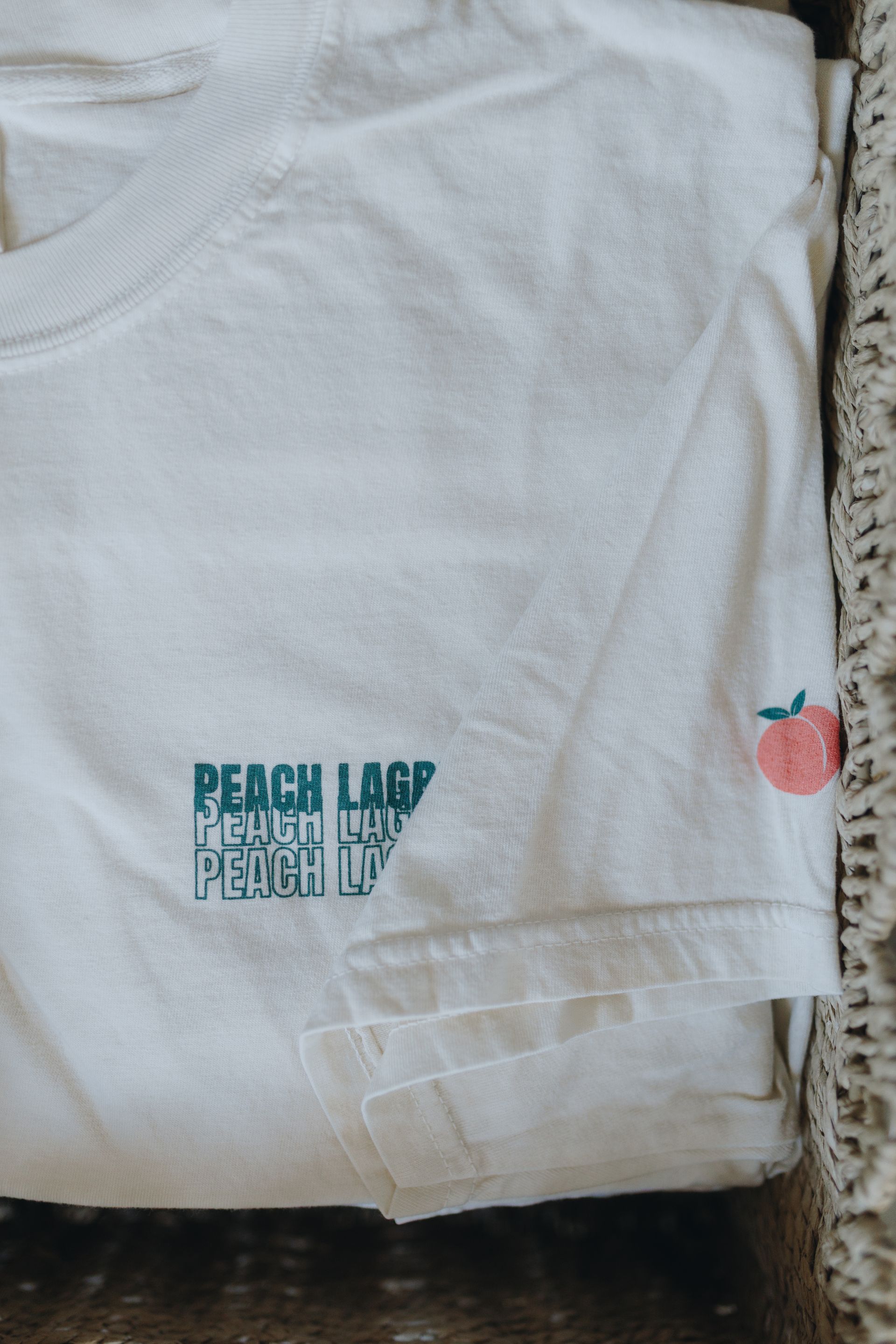 White T-shirt with teal “PEACH LAND” text and a small peach graphic on the right sleeve.