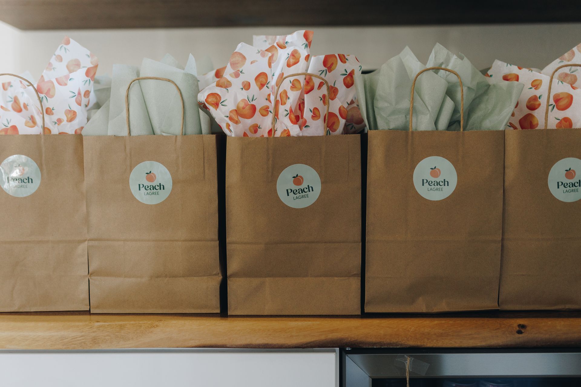 Brown paper gift bags lined up on a shelf, topped with white and orange tissue paper.