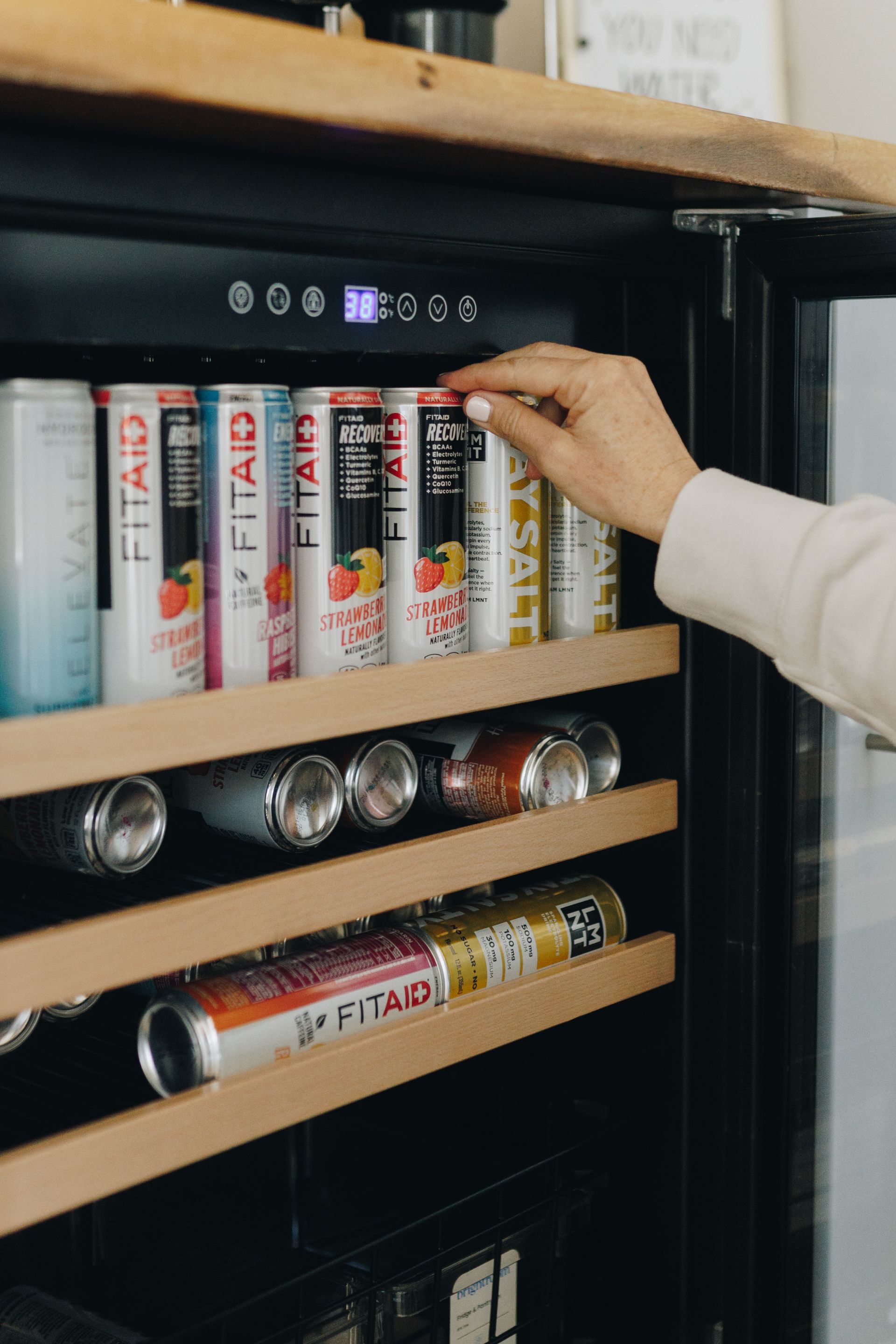 Hand placing a can on a shelf of a vending machine with assorted drinks and snacks