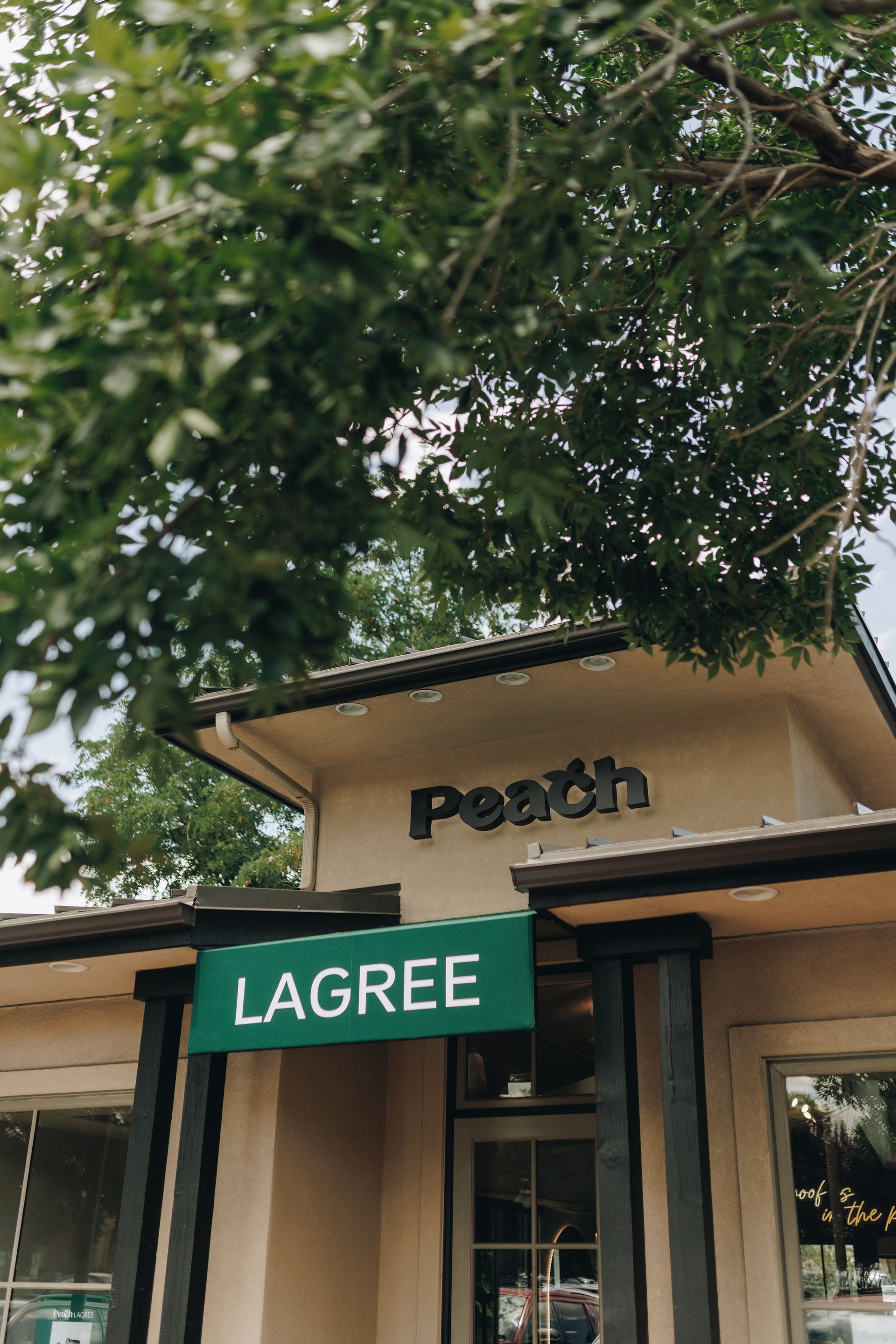 Storefront with green “LAGREE” sign and tree canopy above the entrance