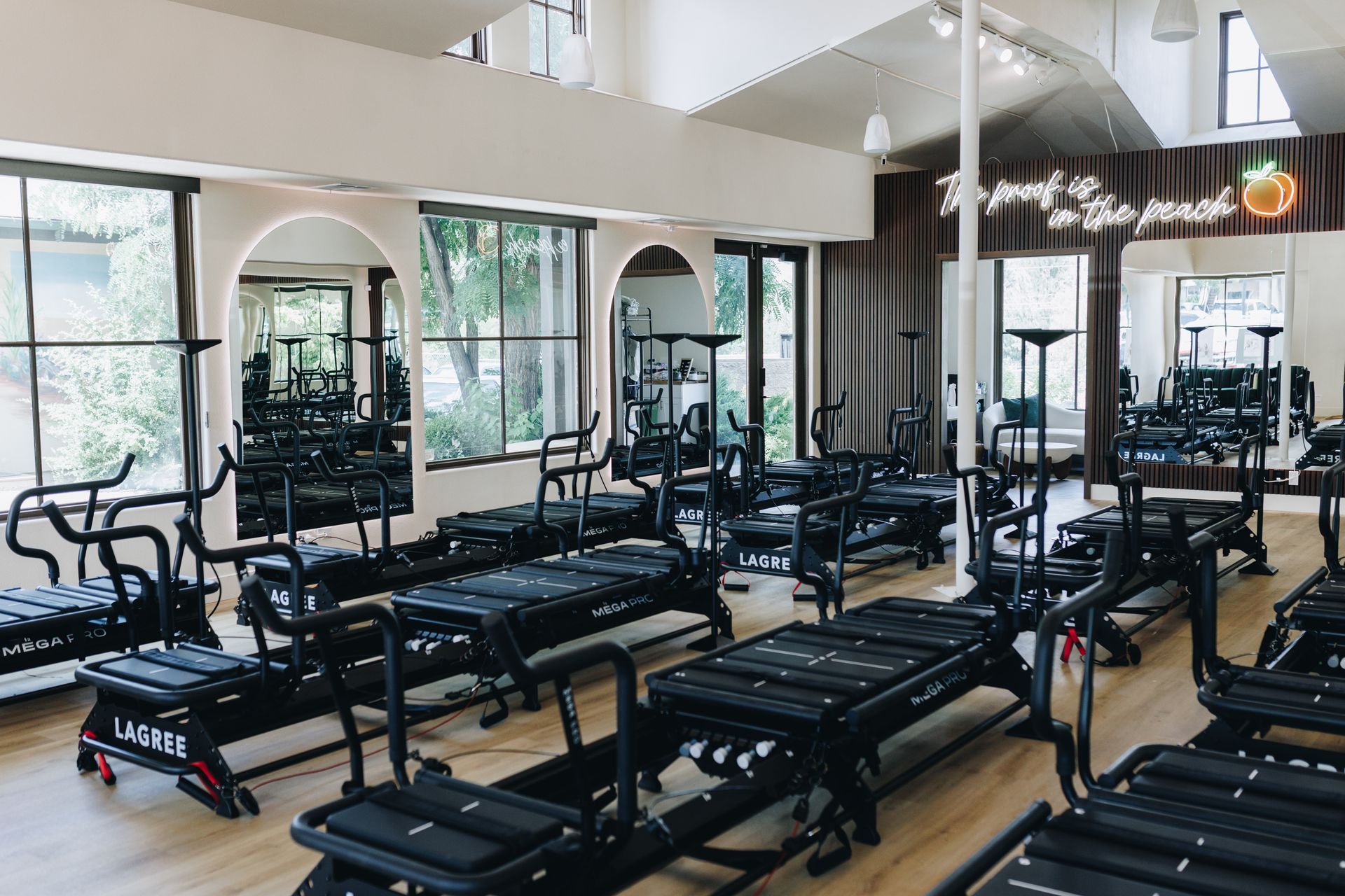 Bright gym with rows of reformer pilates machines, mirrors, and large windows.