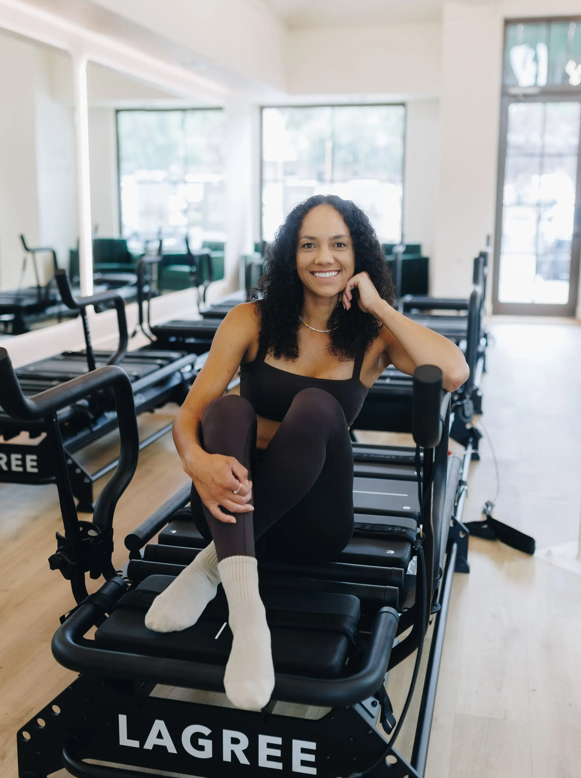 Woman smiling on a black Lagree reformer in a bright fitness studio