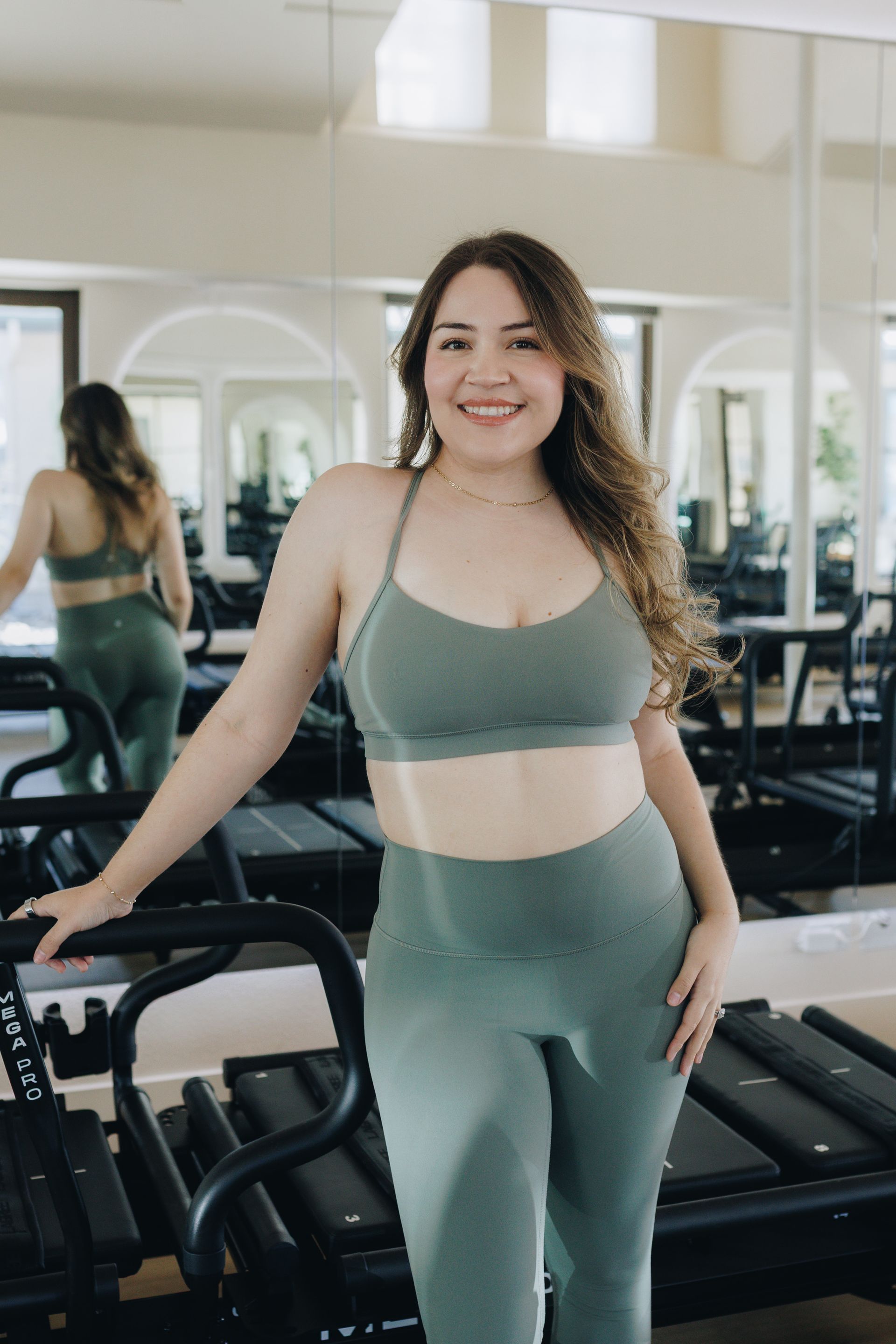 Woman in green workout set posing beside gym equipment in a mirrored fitness studio