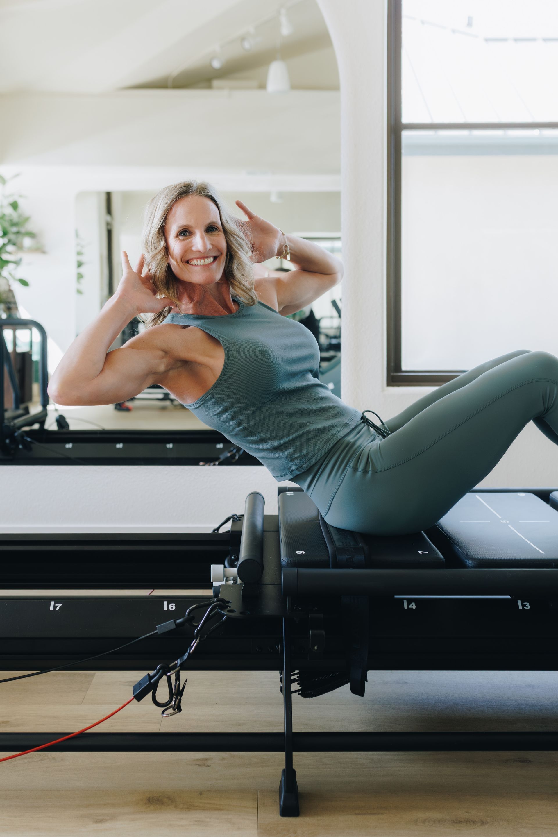 Woman in teal workout clothes exercising on a reformer Pilates machine in a bright studio