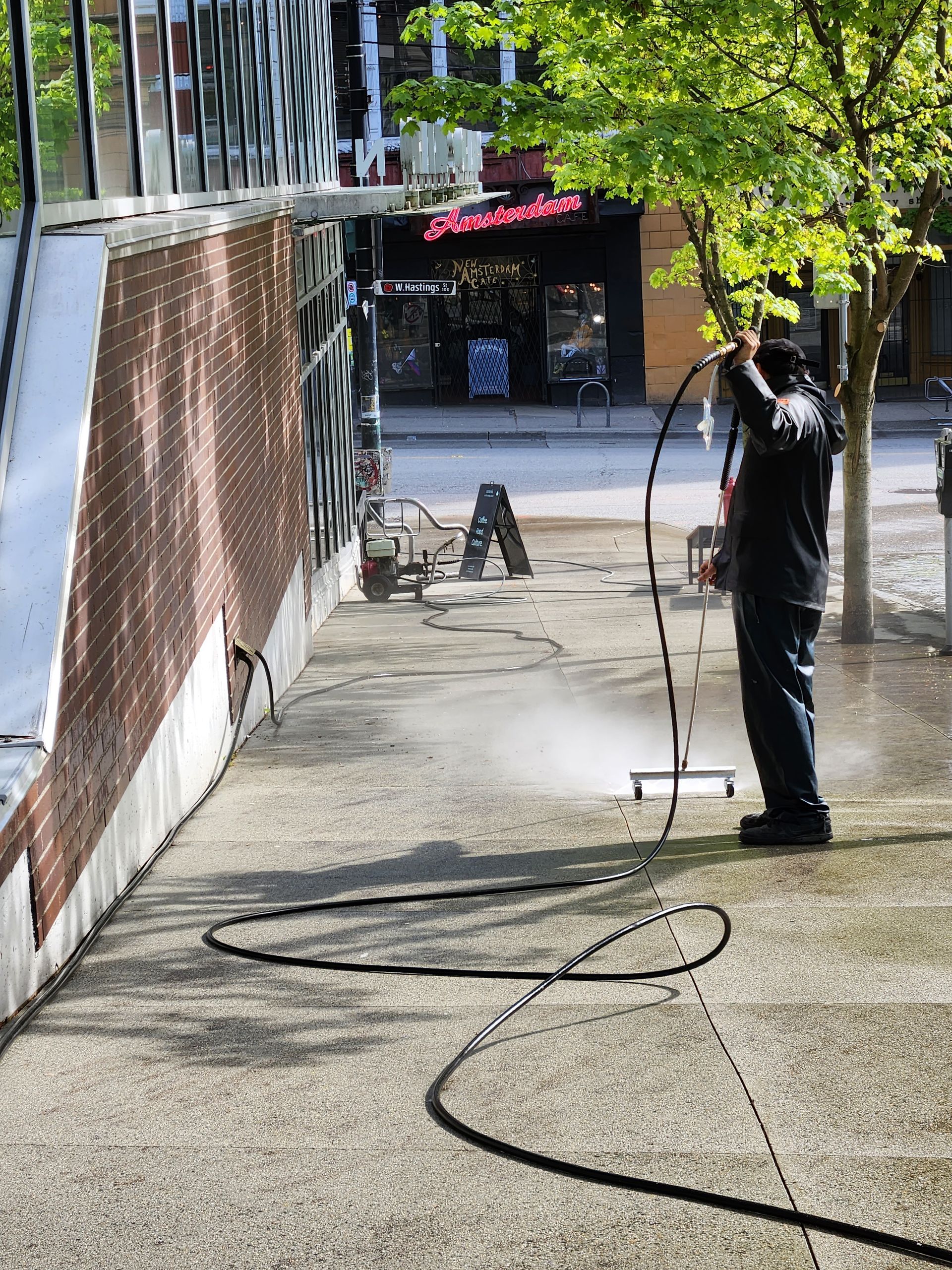 A man is using a high pressure washer to clean a sidewalk.