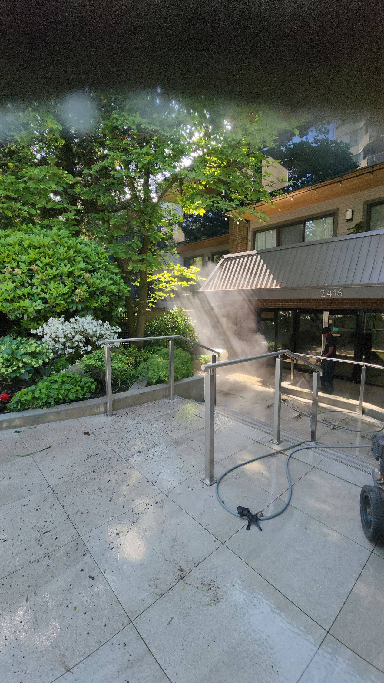 A person is cleaning a patio with a vacuum cleaner in front of a building.