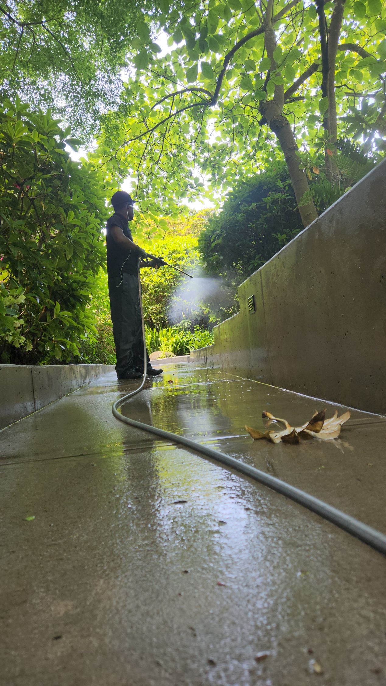 A man is using a high pressure washer to clean a sidewalk.