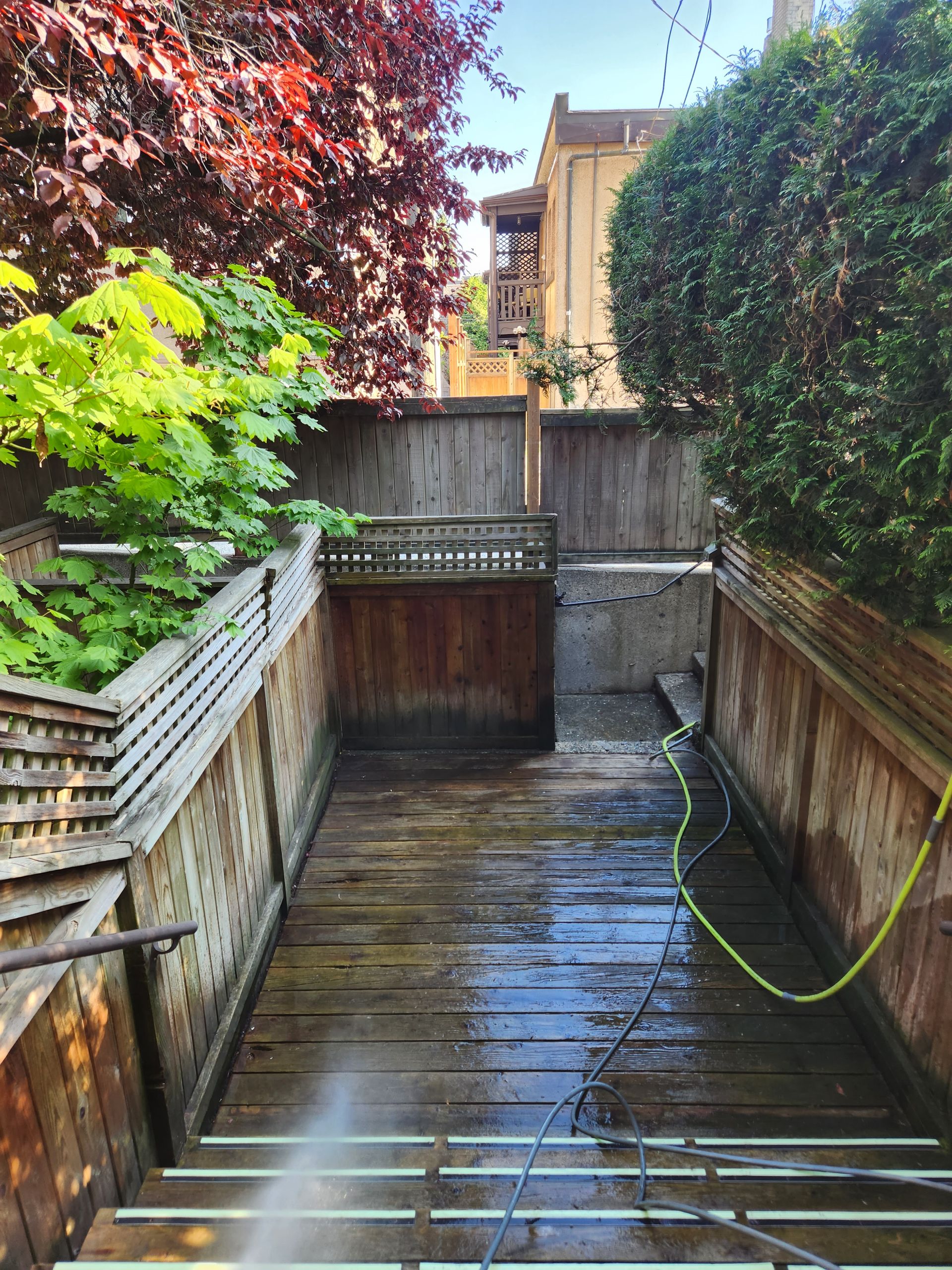 A person is using a high pressure washer to clean a wooden deck.