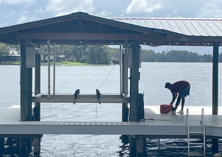 Person on a dock by water, interacting with items next to a covered boat lift. Overcast sky.