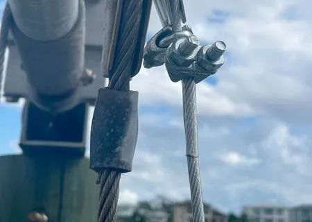 Close-up of metal cable and fasteners against a cloudy sky.