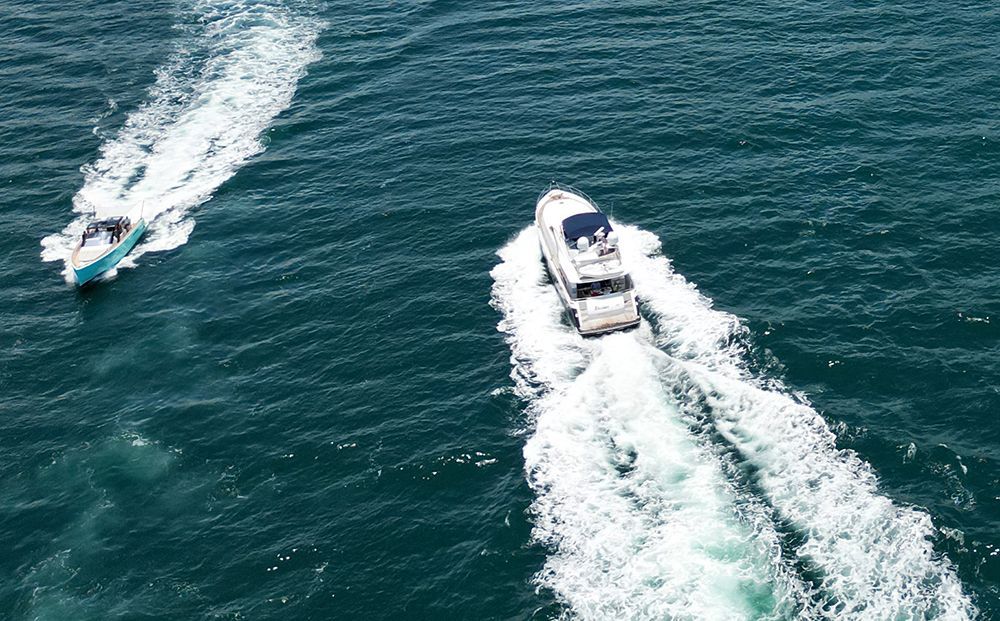 Two motorboats speeding across the ocean, leaving foamy white wakes.
