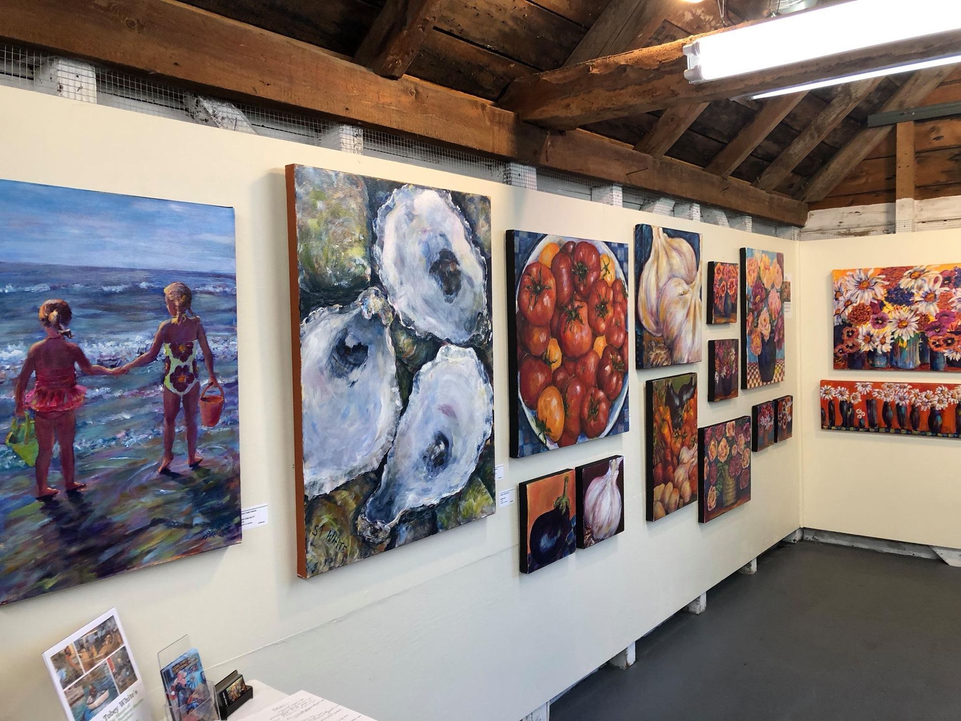 Art gallery wall with colorful paintings displayed in a bright, wood-beamed room