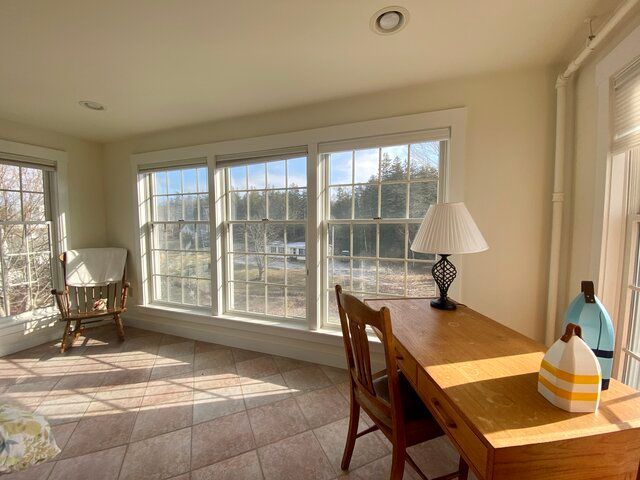 Sunlit room with large windows, tiled floor, and a wooden desk with a lamp and decorative vase.