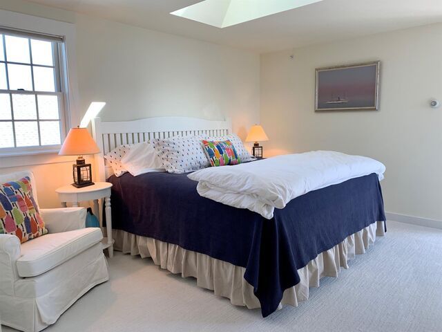 Bright bedroom with a white bed, navy bedspread, pastel chair, and soft lamps under a skylight