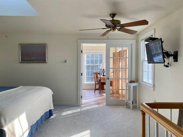 Bedroom with bed, ceiling fan, wall-mounted TV, and French doors leading to a sitting area