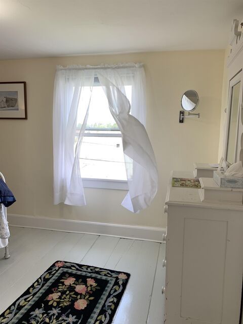 Small beige room with a window, sheer curtains, floral rug, and a white dresser.