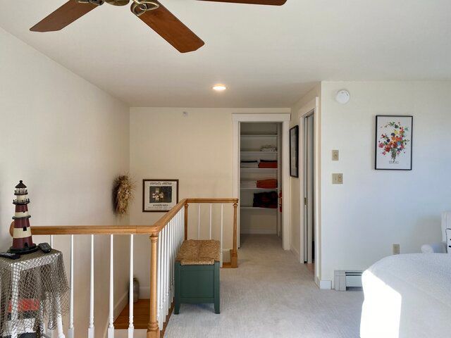 Bright upstairs hallway with railing, ceiling fan, and open doorway to a bedroom.