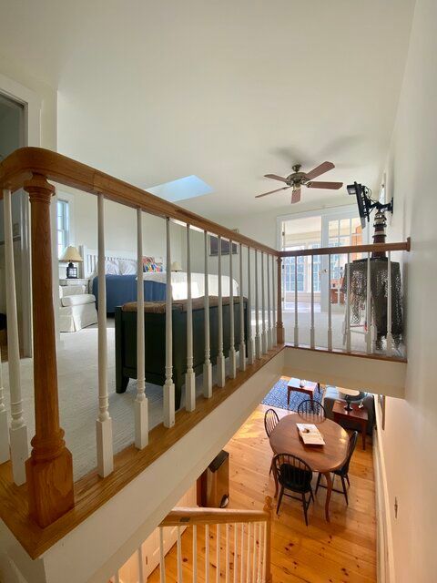 Open loft view with wooden railing, ceiling fan, and a small dining area below.