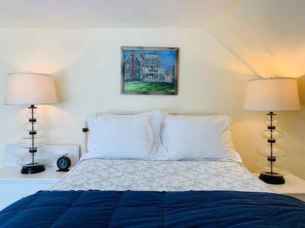 Cozy bedroom with a blue bedspread, bedside lamps, and framed art on a white wall