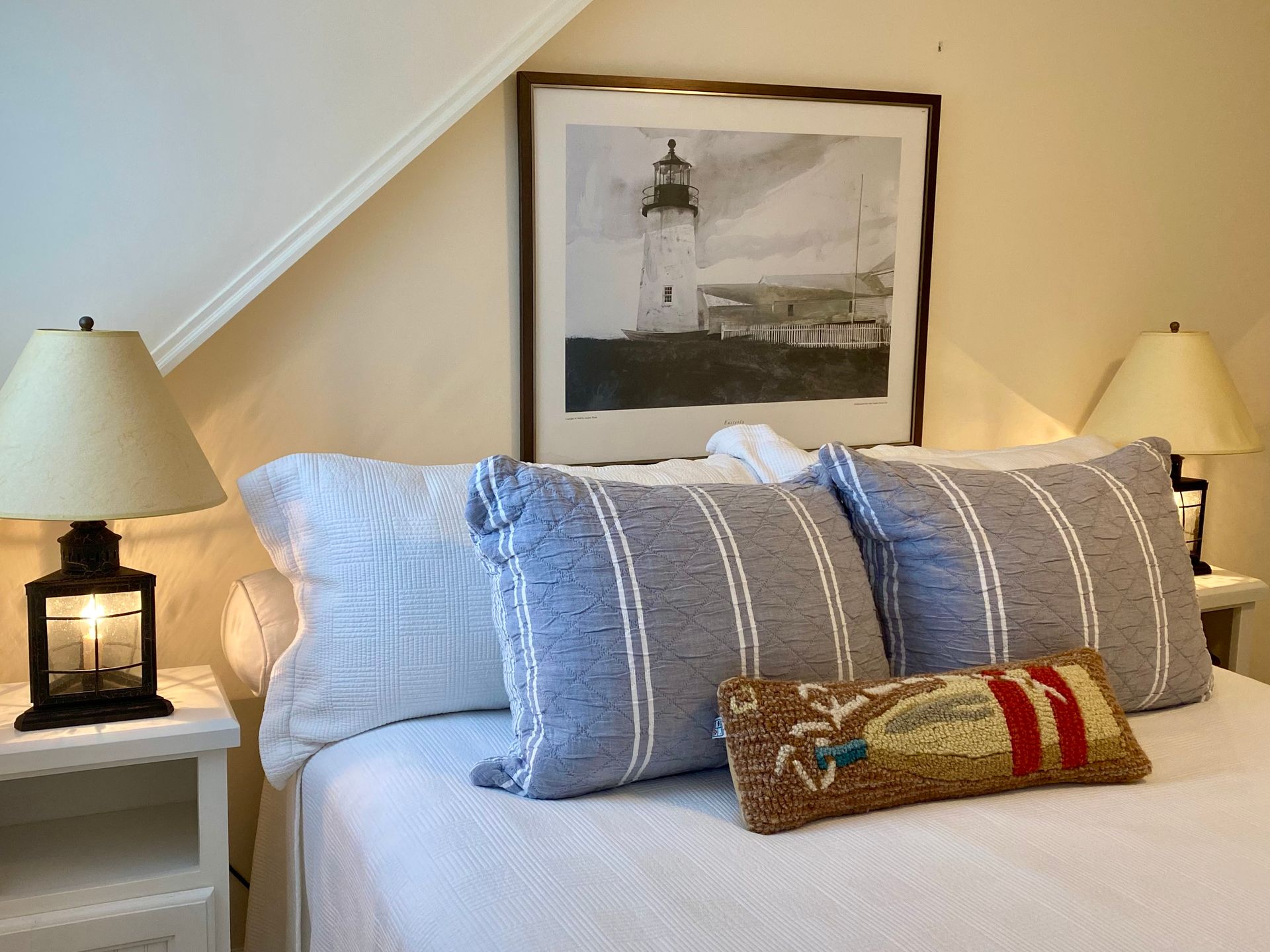 Cozy bedroom with neatly made bed, blue striped pillows, bedside lamps, and framed wall art