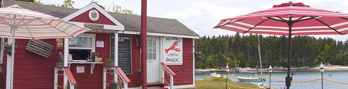 Red seaside kiosk with a pink umbrella beside calm water and docked boats