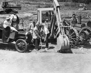 Workers with a backhoe and truck clearing dirt on a rural road.