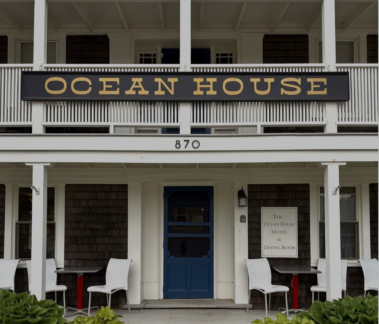 Storefront of Ocean House with white columns, blue door, and porch seating