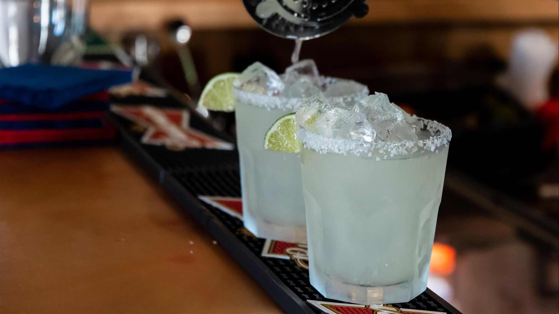 Two icy cocktails in short glasses with lime wedges on a bar counter