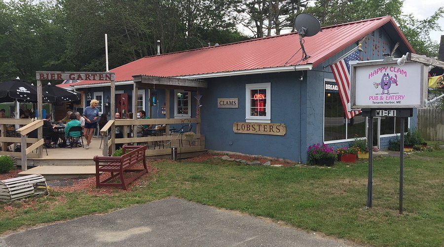 Small blue café with red roof, porch seating, and a roadside sign in a grassy lot.