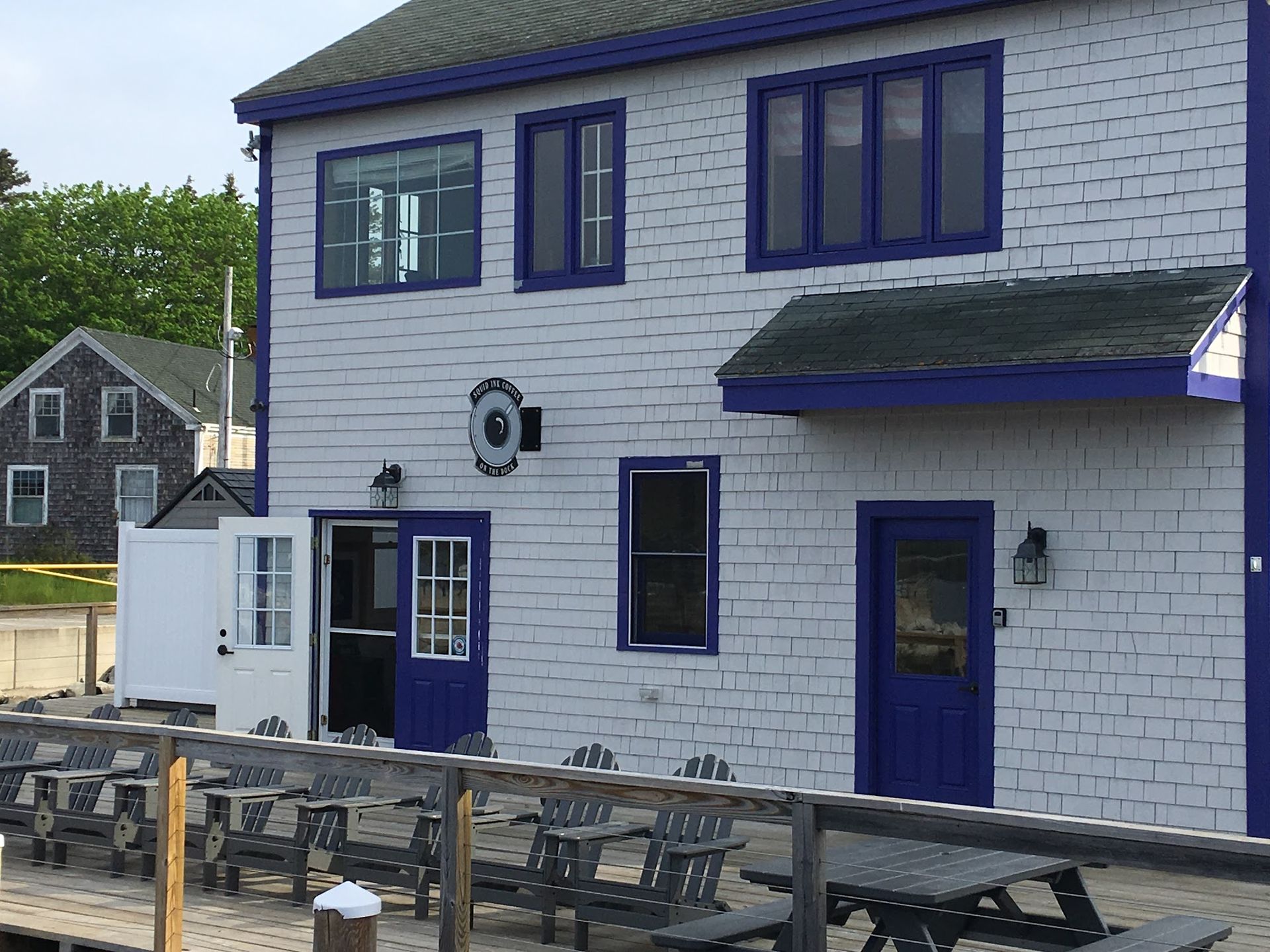 White brick building with blue trim, windows, doors, outdoor tables, and a patio by the roadside.